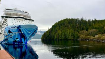 Norwegian Cruise Line ship docked near forested Alaskan coastline