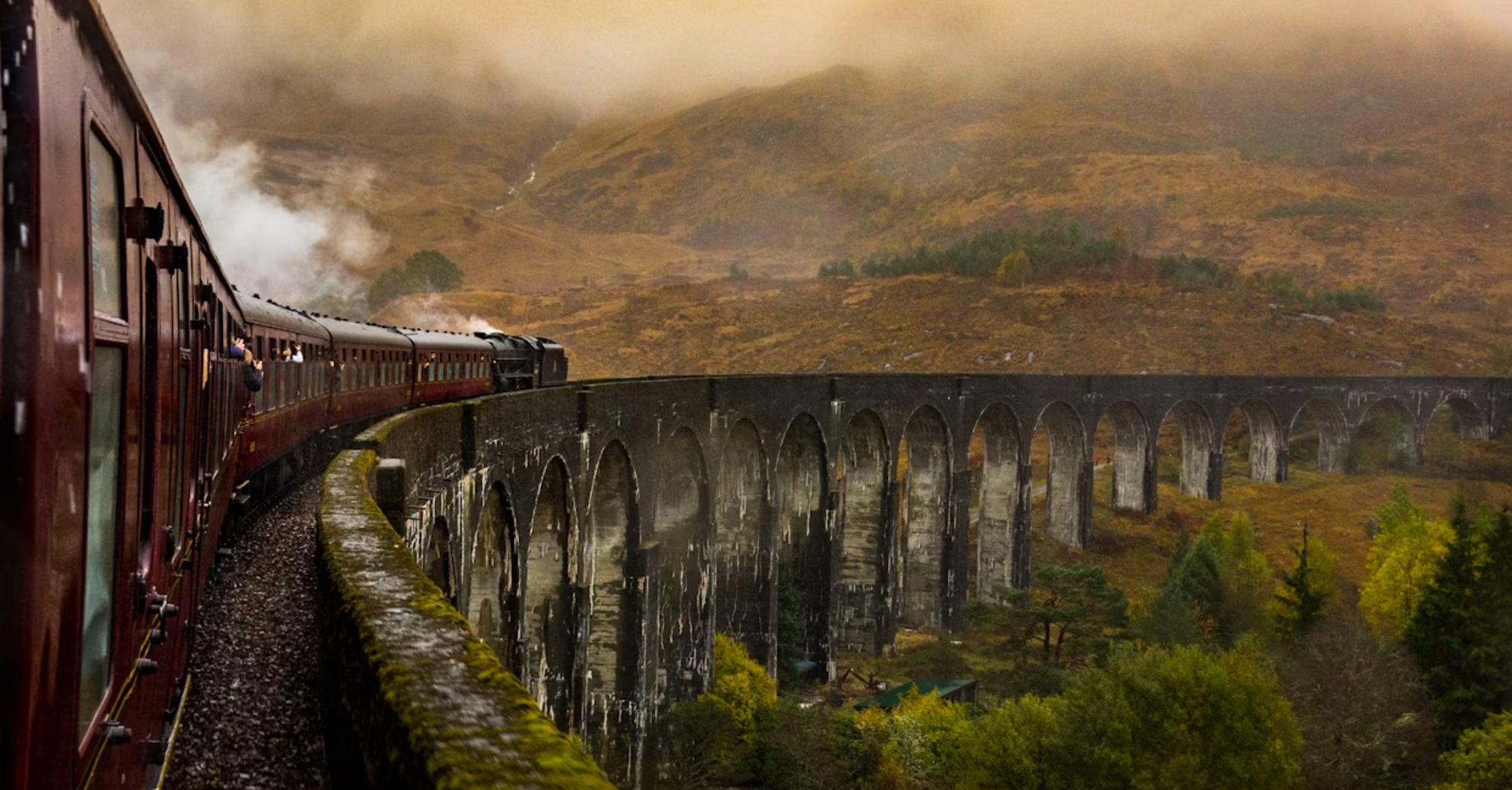 Steam train crossing a historic stone viaduct through misty hills