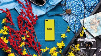 Smartphone with eSIM logo surrounded by travel essentials like flowers, map, camera, and sunglasses