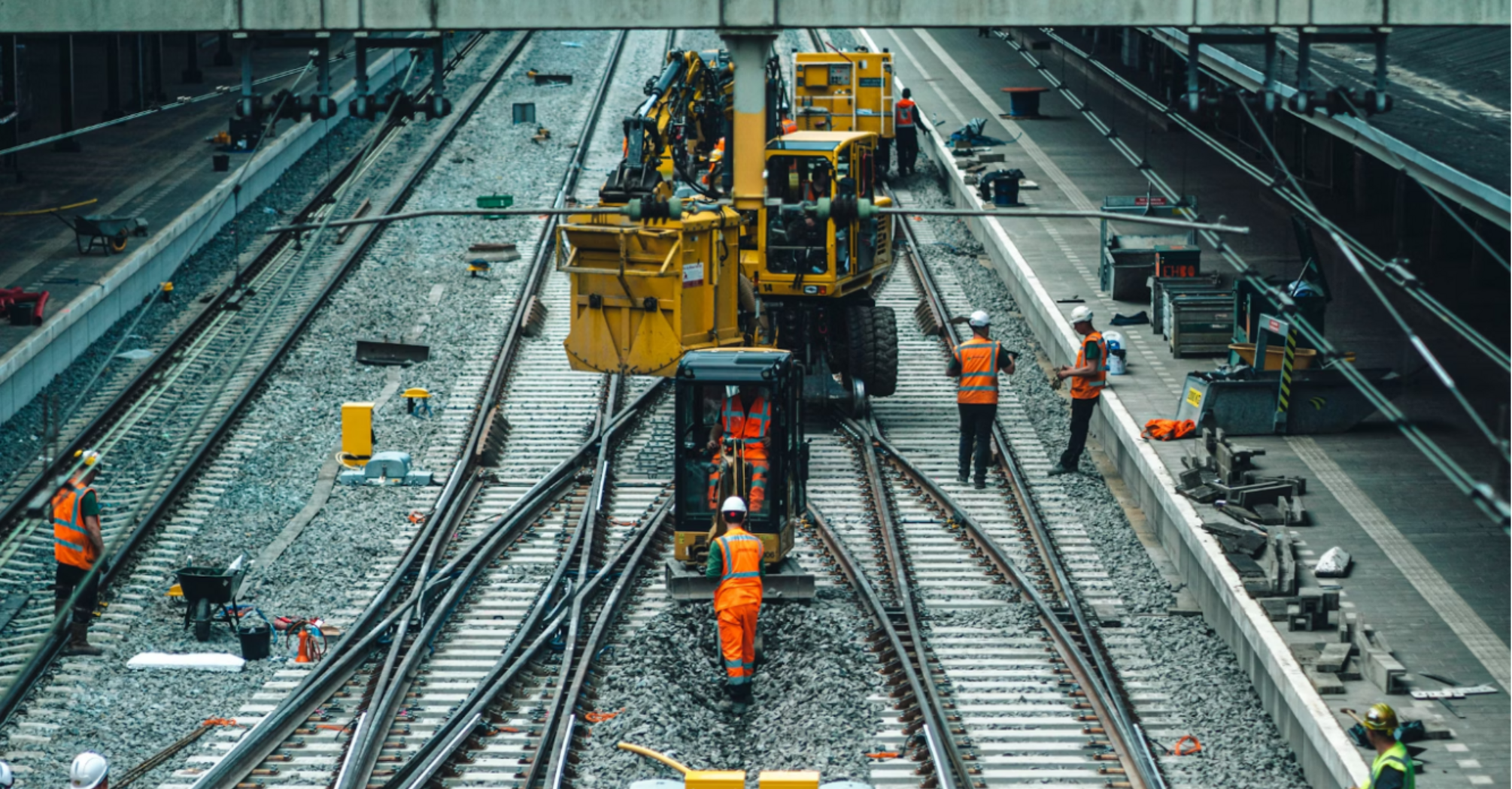 Railway workers and machinery performing track maintenance at a train station