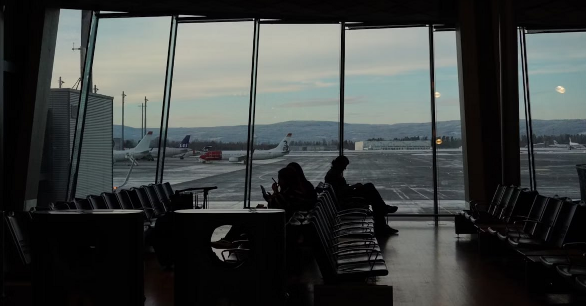 Passengers waiting at Oslo Gardermoen Airport gate with planes outside