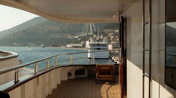 Empty deck of a cruise ship docked in a coastal European port with hills and a bridge in the background