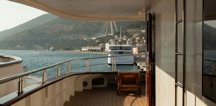 Empty deck of a cruise ship docked in a coastal European port with hills and a bridge in the background