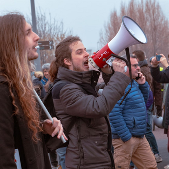 A man shouting into a megaphone during a protest with a crowd in the background