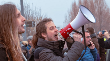 A man shouting into a megaphone during a protest with a crowd in the background