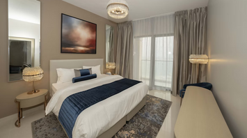 Modern hotel room with neutral tones, large bed, and floor-to-ceiling curtains