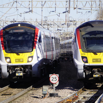Two Greater Anglia trains at a station under overhead electric lines