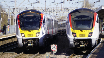 Two Greater Anglia trains at a station under overhead electric lines