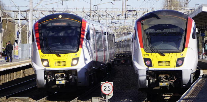 Two Greater Anglia trains at a station under overhead electric lines