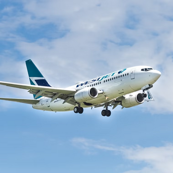 WestJet airplane landing with extended flaps against blue sky