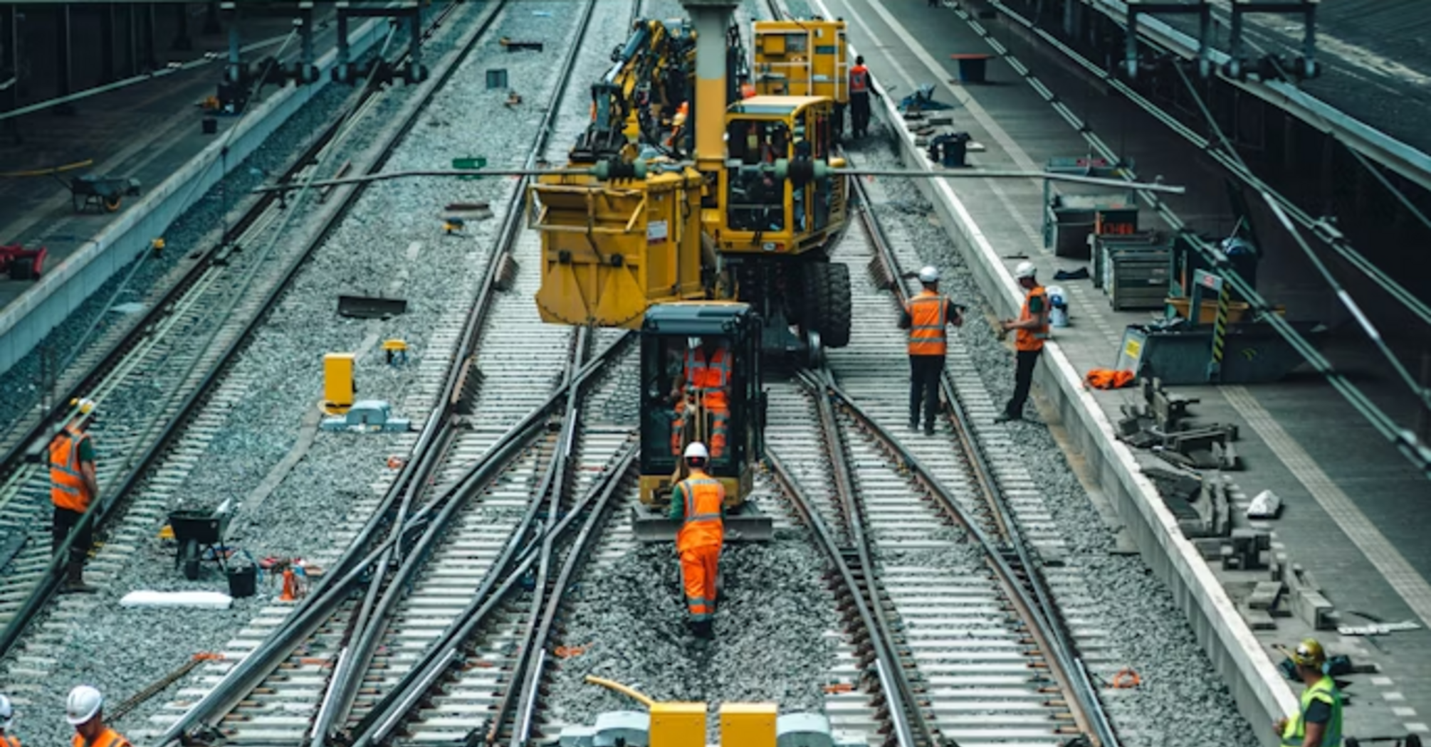 Rail workers performing track maintenance at a train station during daytime