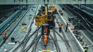 Rail workers performing track maintenance at a train station during daytime