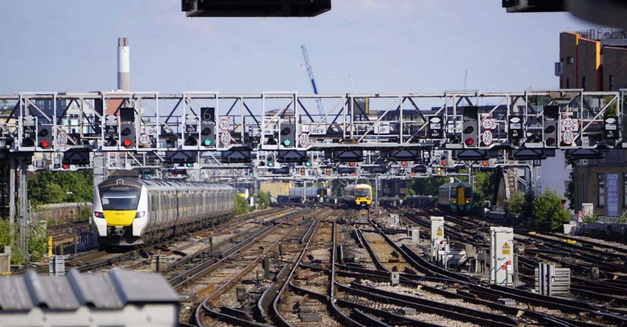 Multiple trains approaching a busy railway junction under signal gantries on a sunny day