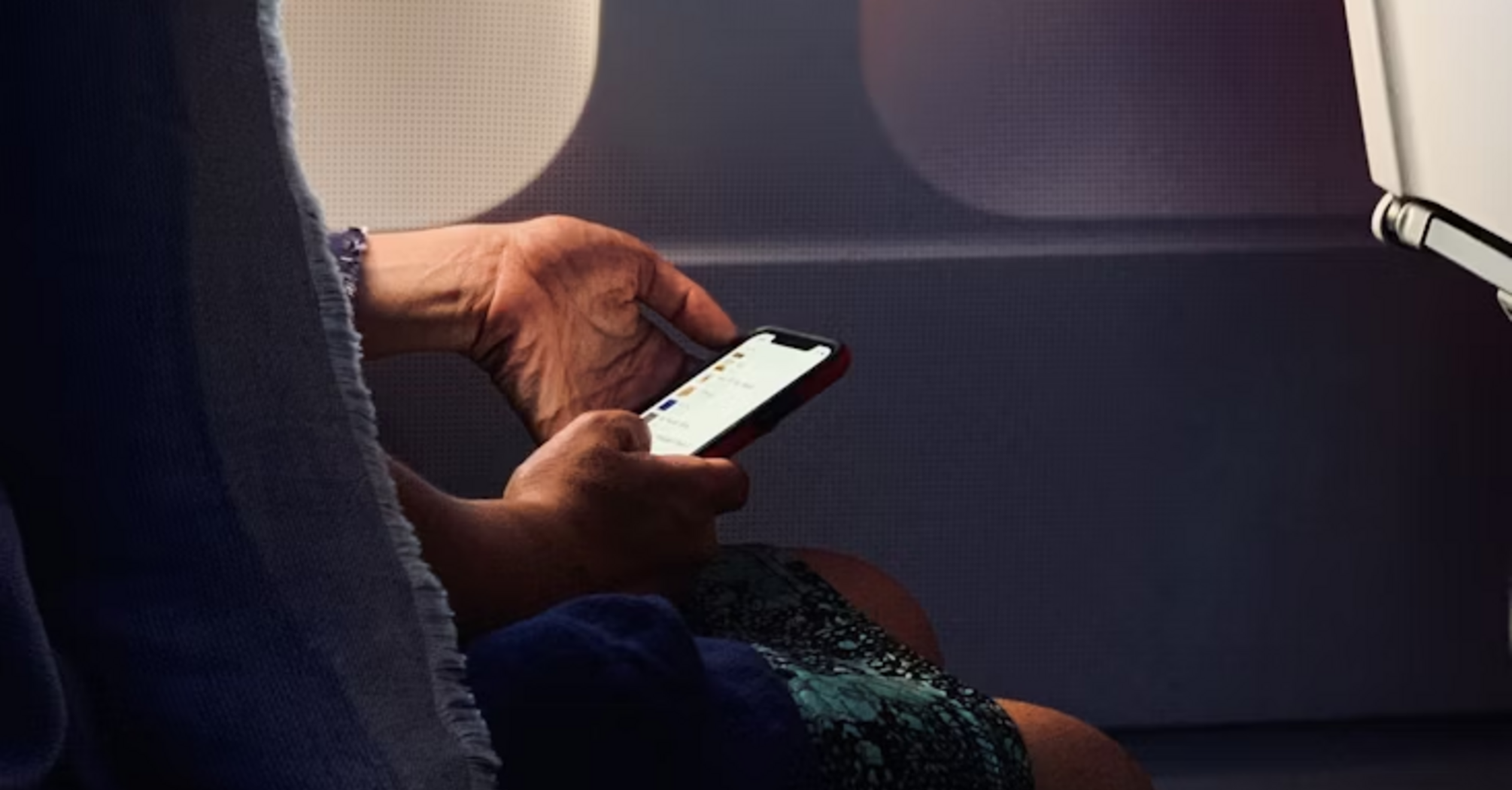 Passenger using smartphone on airplane with window light