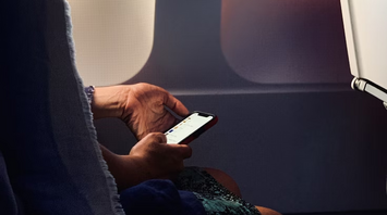 Passenger using smartphone on airplane with window light