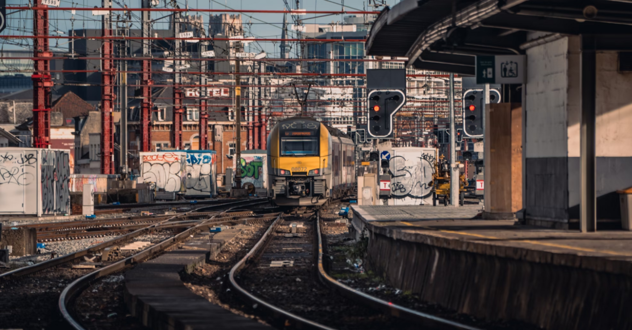 Train approaching a station with multiple tracks and overhead power lines