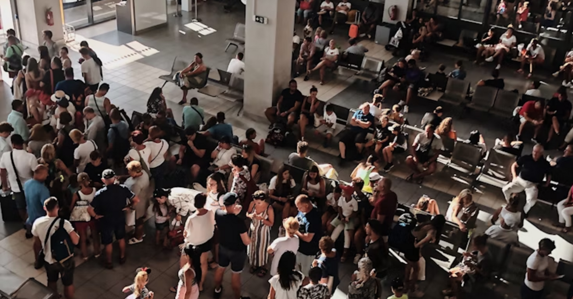 Large crowd of passengers waiting inside a bright terminal with seating areas and boarding gates