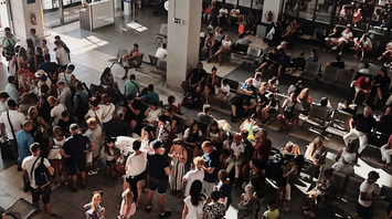 Large crowd of passengers waiting inside a bright terminal with seating areas and boarding gates