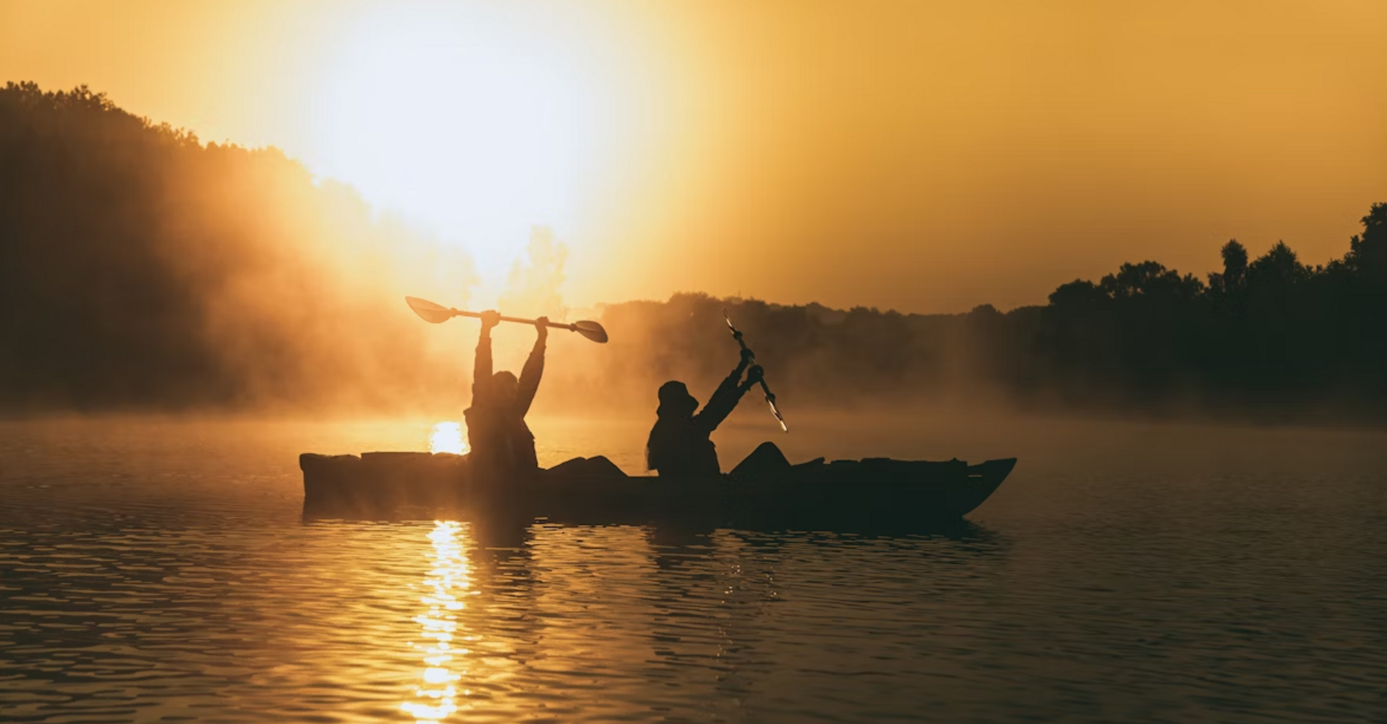 Two people kayaking at sunrise with mist over the water