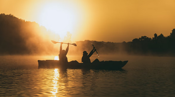 Two people kayaking at sunrise with mist over the water