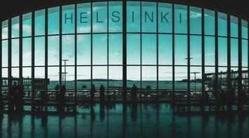 Silhouettes of travelers inside Helsinki Airport terminal with large window view