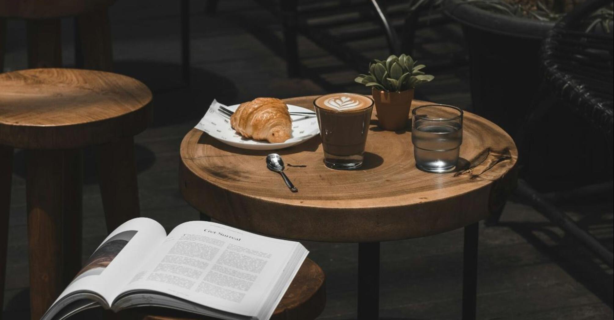 Coffee and croissant on a wooden table with open book