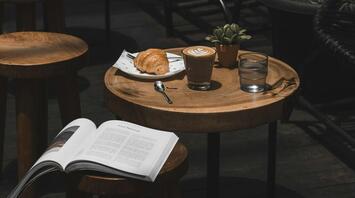 Coffee and croissant on a wooden table with open book