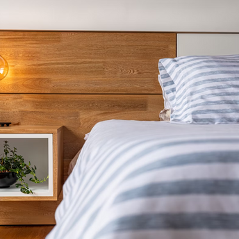 Modern bedroom interior with striped bedding, wooden headboard, and a hanging light bulb