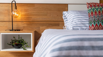 Modern bedroom interior with striped bedding, wooden headboard, and a hanging light bulb