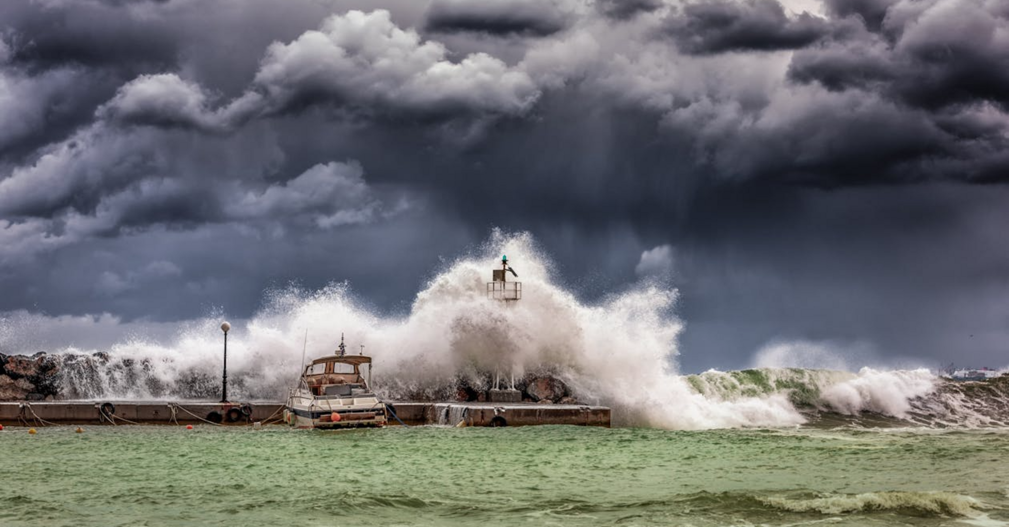 Waves crashing over a harbor wall during a severe storm under dark clouds