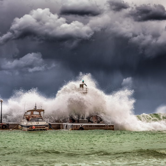 Waves crashing over a harbor wall during a severe storm under dark clouds