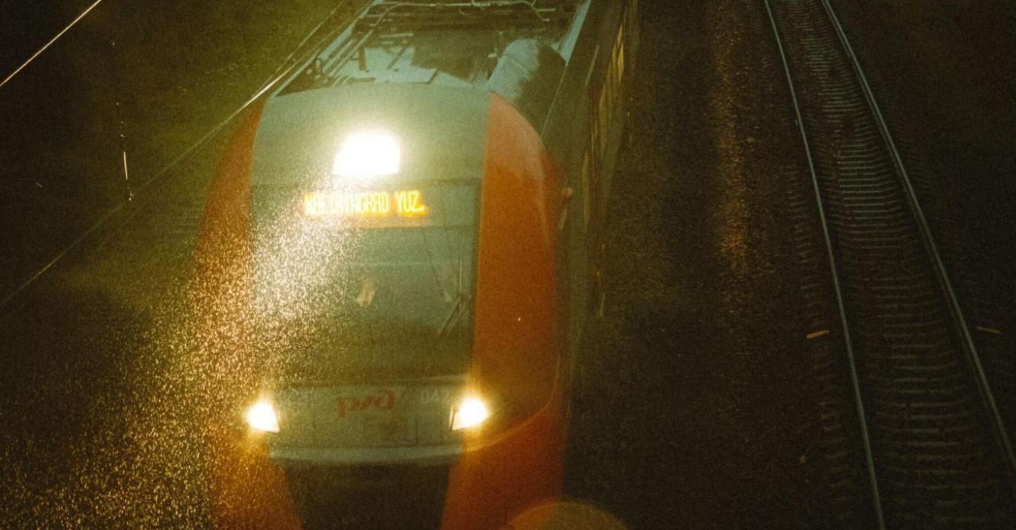 A night train traveling on wet railway tracks under dim evening lights