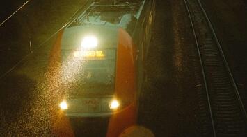 A night train traveling on wet railway tracks under dim evening lights