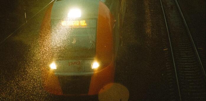A night train traveling on wet railway tracks under dim evening lights