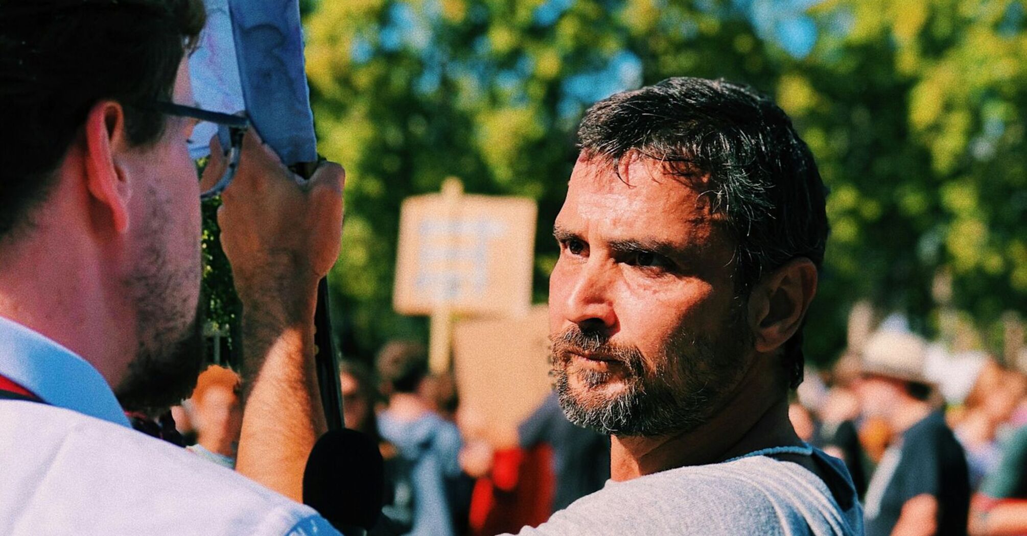 Man with banner at protest talking to reporter