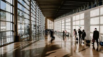 Passengers walking through a bright airport corridor with luggage