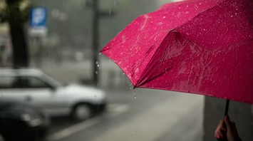 Person holding a red umbrella in heavy rain on a city street