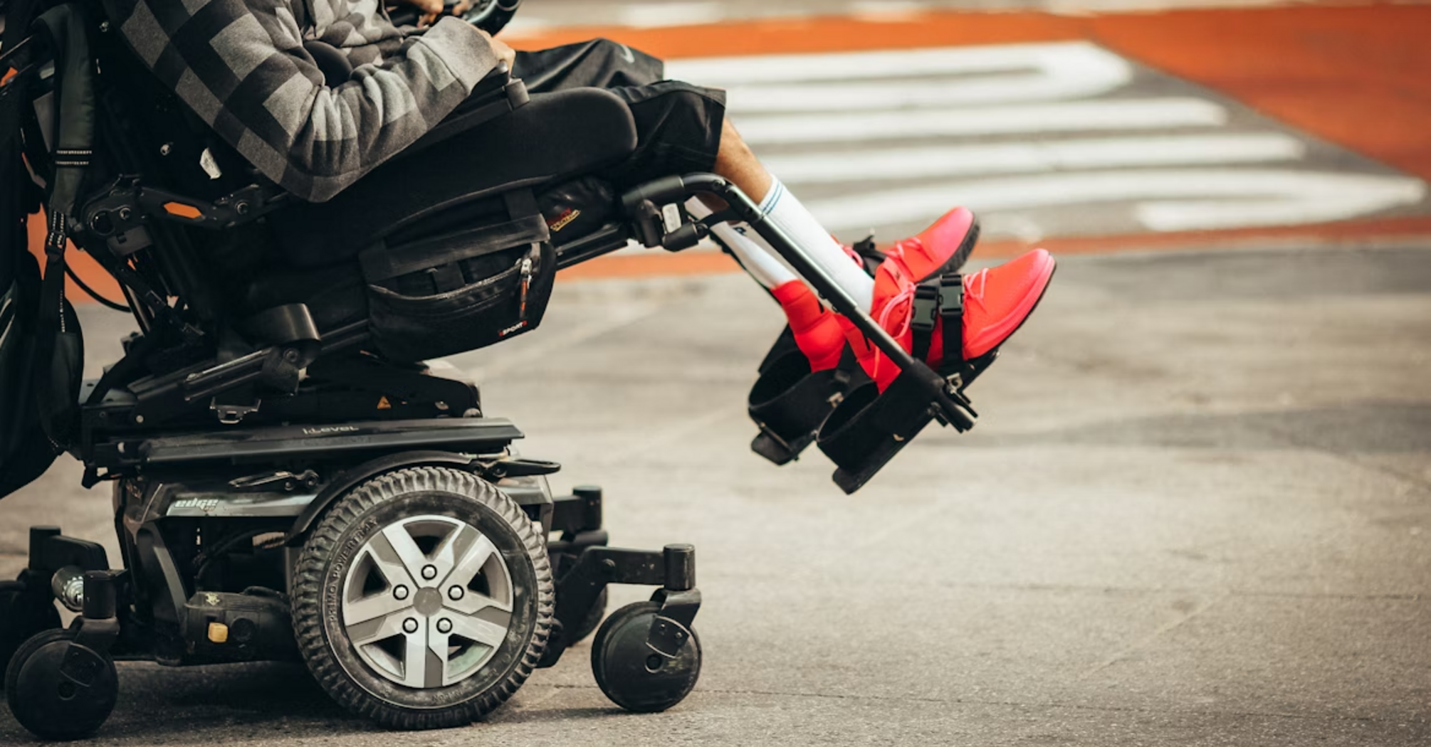 A person using a motorized wheelchair with bright red shoes visible on a city street