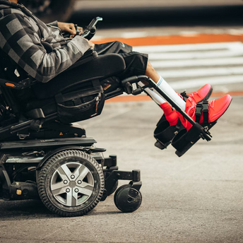 A person using a motorized wheelchair with bright red shoes visible on a city street