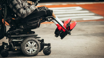 A person using a motorized wheelchair with bright red shoes visible on a city street