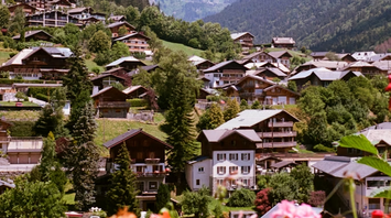 Traditional wooden chalets in the Alpine town of Morzine, surrounded by forested mountains and summer flowers