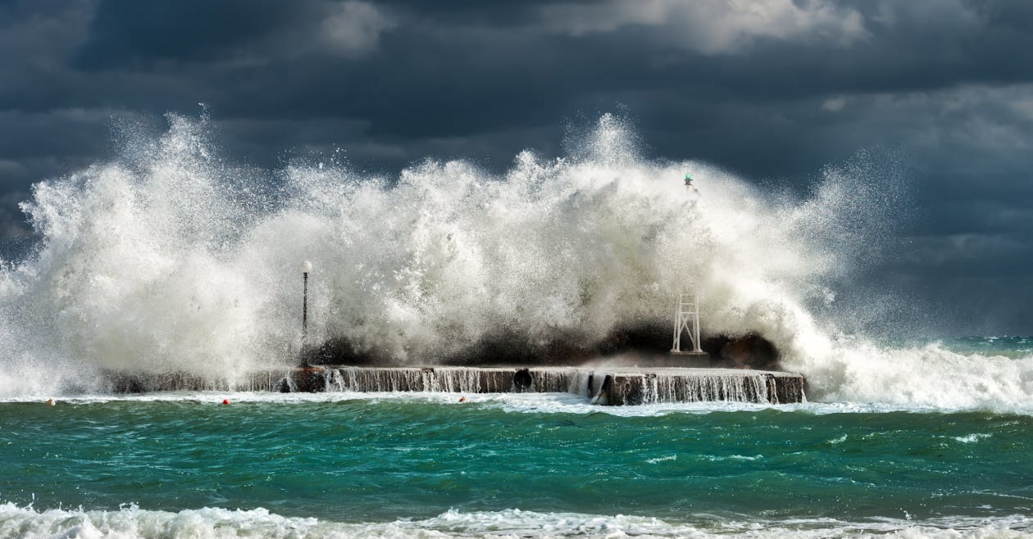 Waves crashing against a coastal barrier during a storm under dark skies