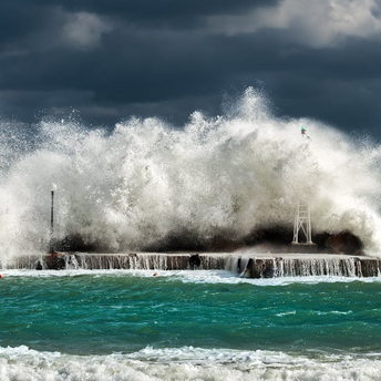 Waves crashing against a coastal barrier during a storm under dark skies