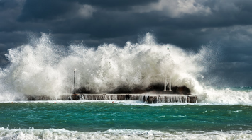 Waves crashing against a coastal barrier during a storm under dark skies