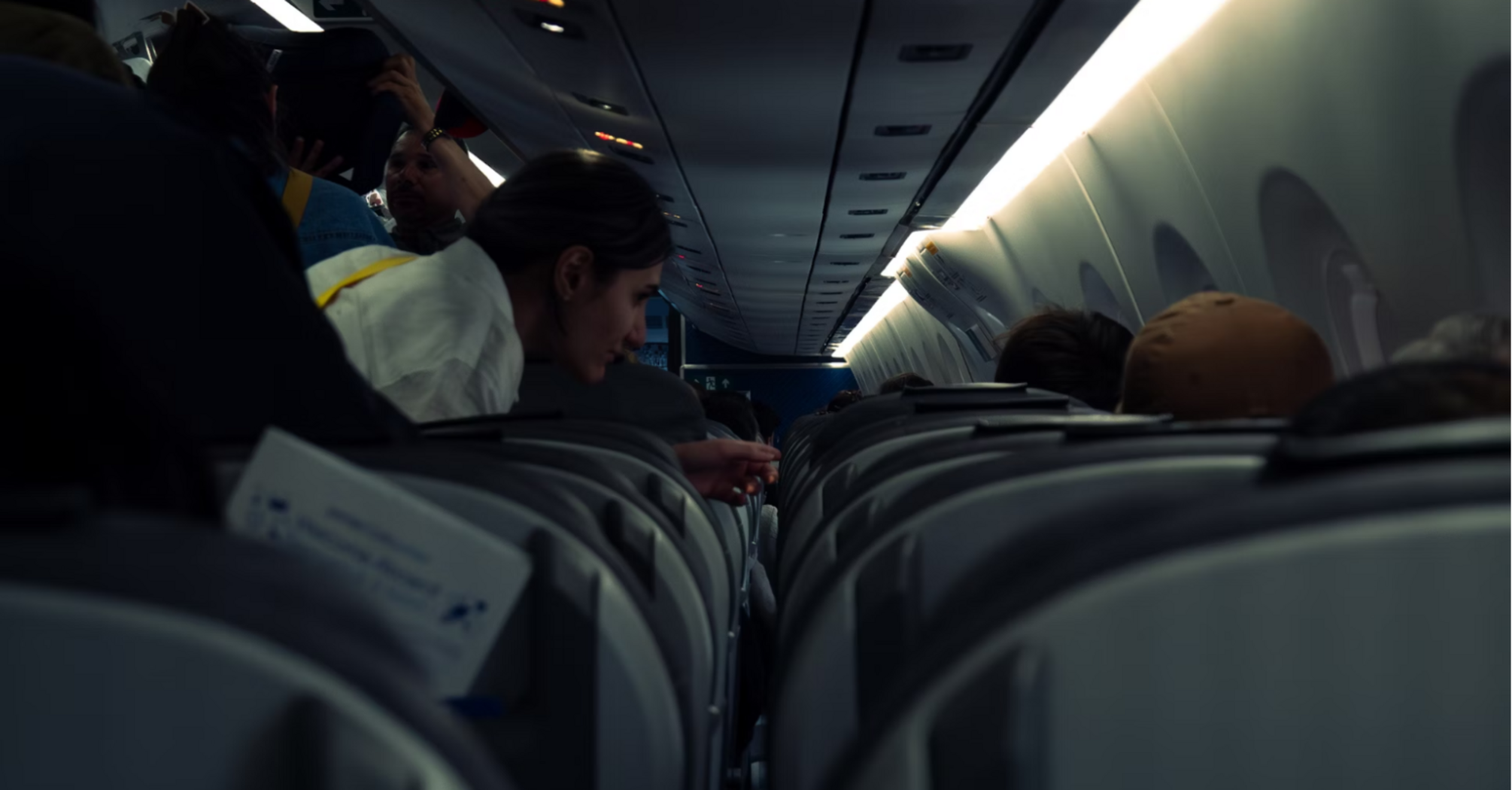 Passengers seated and standing inside a dimly lit airplane cabin