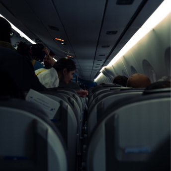 Passengers seated and standing inside a dimly lit airplane cabin