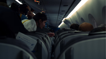 Passengers seated and standing inside a dimly lit airplane cabin