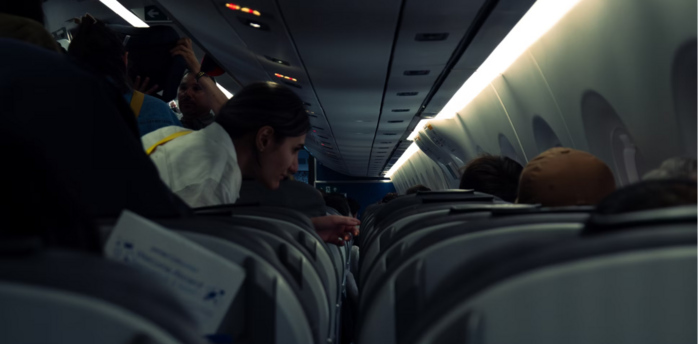 Passengers seated and standing inside a dimly lit airplane cabin