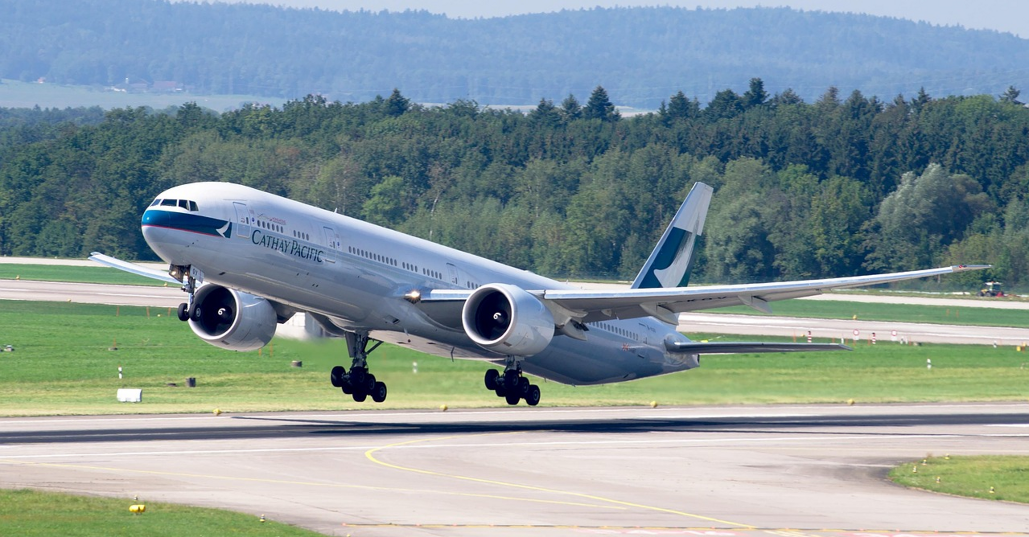 Cathay Pacific aircraft taking off from a runway surrounded by greenery