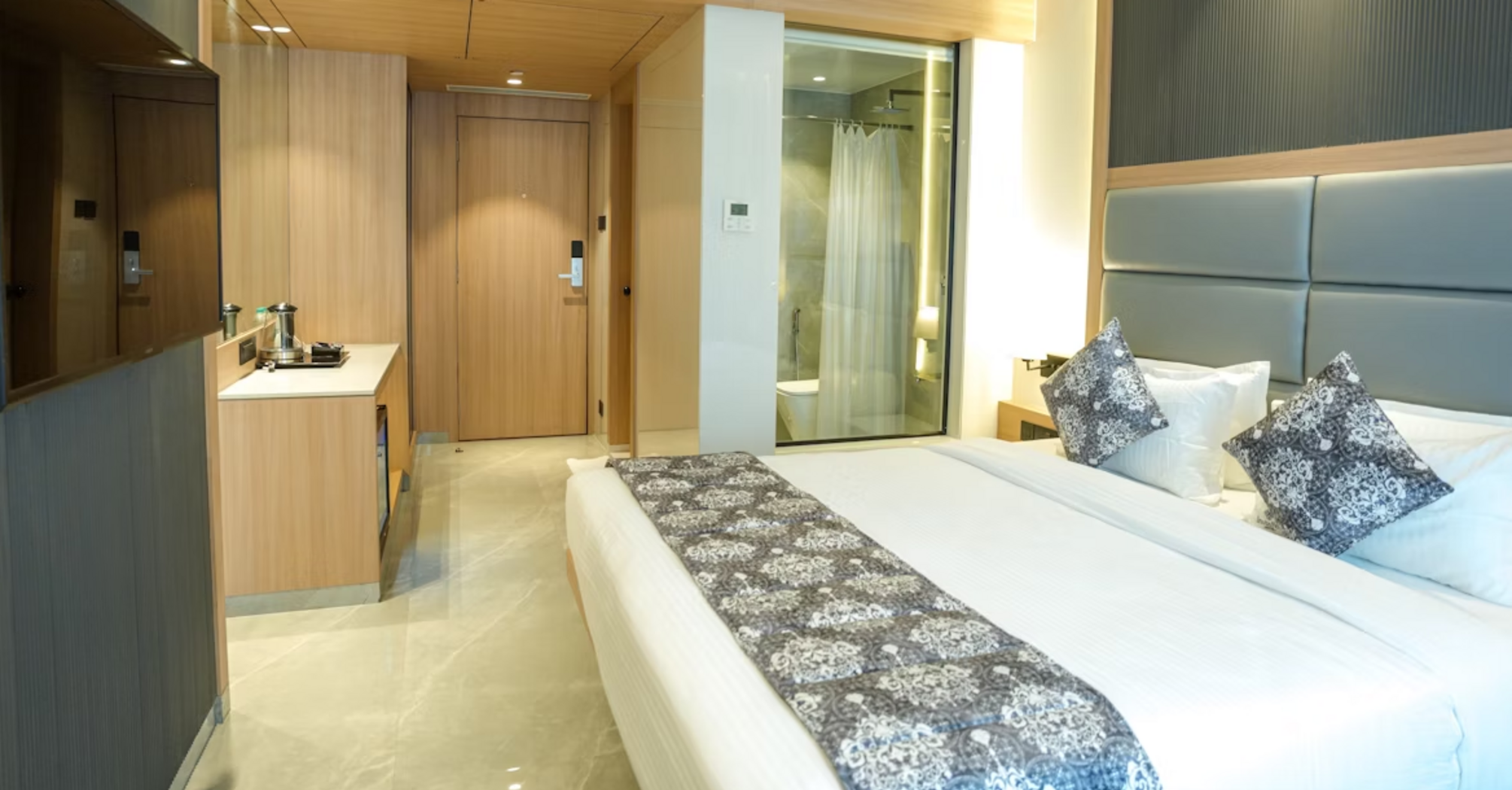 Modern hotel bedroom with neutral tones and glass-walled bathroom